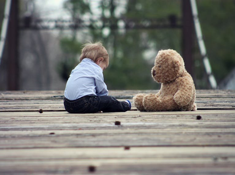 Adorable toddler sitting with a teddy bear on a wooden bridge, enjoying a peaceful moment outdoors.