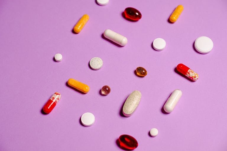 A variety of colorful pills and tablets scattered on a vivid purple background for healthcare and medicine themes.