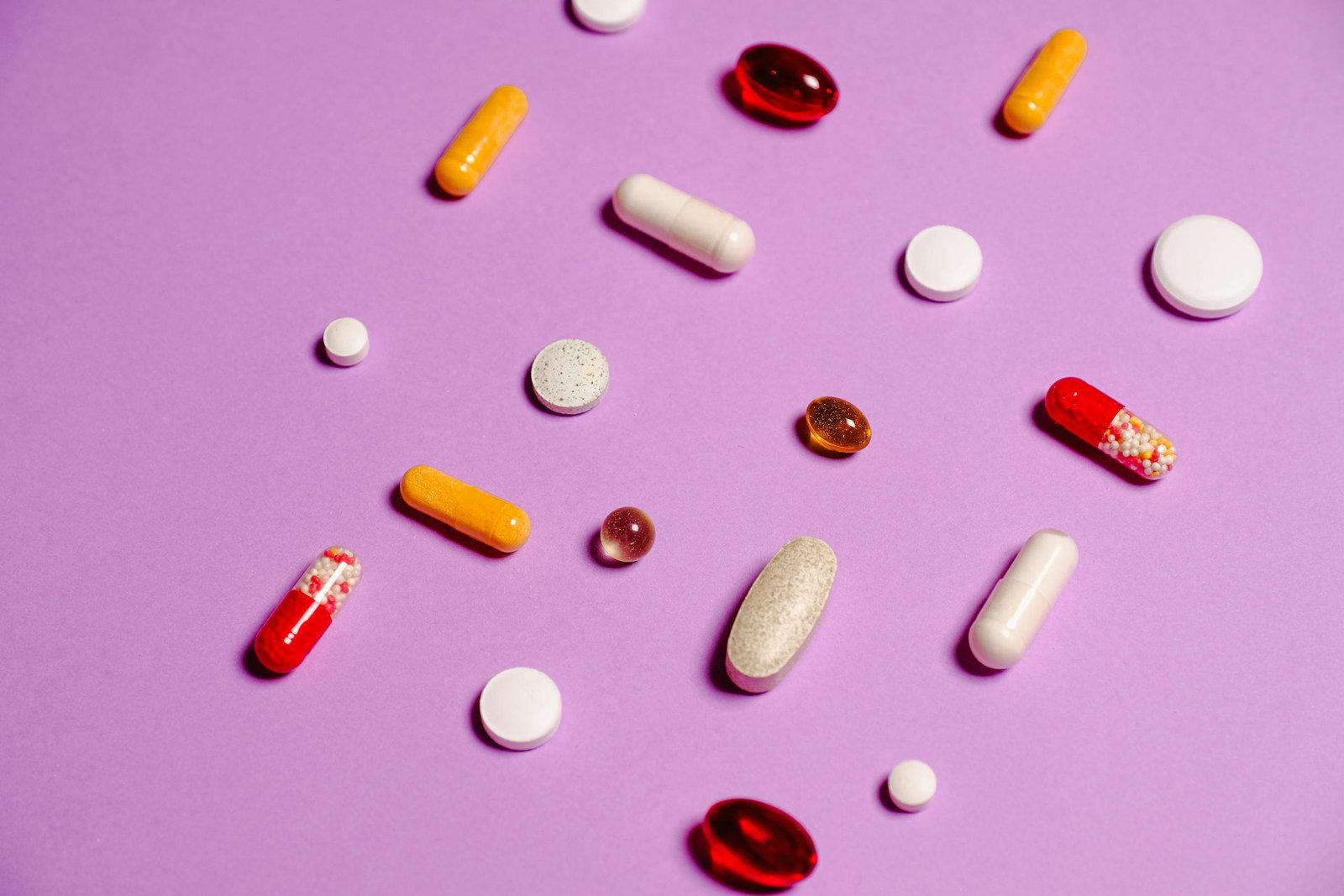 A variety of colorful pills and tablets scattered on a vivid purple background for healthcare and medicine themes.