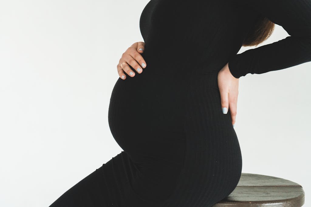 Close-up of a pregnant woman in a black dress holding her back, showcasing her pregnancy bump.